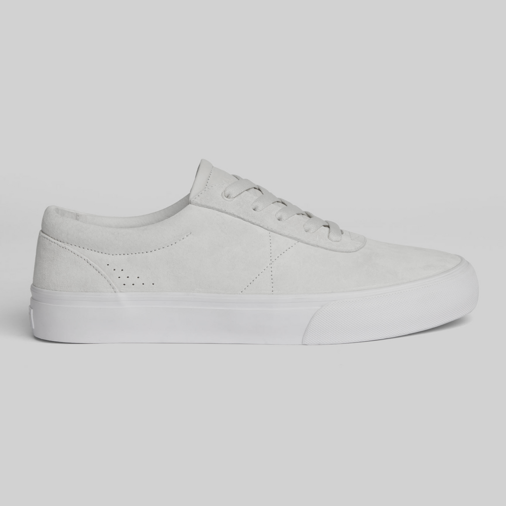 The WARSAW LTD CHAPTER | WHITE / WHITE is a white low-top sneaker with laces, side perforations, and a plain rubber sole, featuring a minimalistic silhouette shown in side profile against a light background.