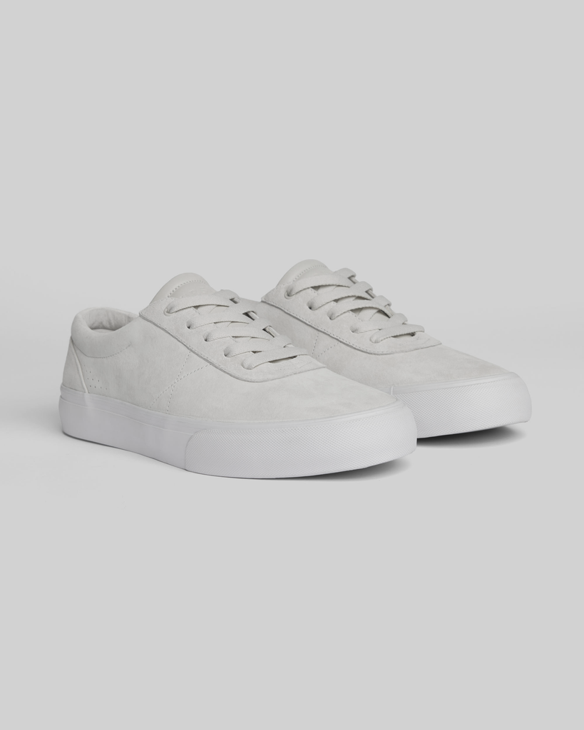 The CHAPTER | WHITE / WHITE sneakers by WARSAW LTD are minimalistic low-tops with white laces and rubber soles, shown on a light gray background.