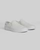 The WARSAW LTD STRANGER SLIP-ON | WHITE / WHITE features genuine pig suede in light gray, white rubber soles, and a minimal silhouette, displayed on a plain light background.