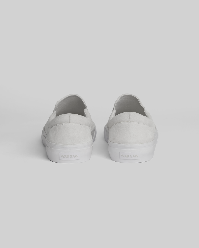 The STRANGER SLIP-ON sneakers by WARSAW LTD in white are shown from the back, highlighting their minimalistic silhouette against a plain light background.