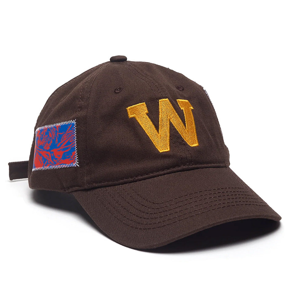 The WKND EDDY HAT BROWN by WKND features a bold yellow "W" embroidered on the front and a blue and red rectangular patch on the side.