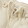 Close-up of Butter Goods Weathergear Heavy Weight Denim Jeans in washed khaki with white drawstrings in the belt loops, orange stitching, a button marked "BUTTER GOODS" on the waistband, and a label partly visible below the button. The baggy fit adds a relaxed appeal to these stylish jeans.