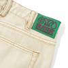 A close-up of the Butter Goods Weathergear Heavy Weight Denim Jeans in washed khaki, featuring an embroidered green "Butter Weathergear" label above the back pocket, showcasing their baggy fit.