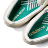 Close-up of two white ADIDAS X ARROW & BEAST SUPERSTAR ADV WONDER WHITE/CRYSTAL WHITE skate shoes, showing green insoles with "ARROW & BEAST" and "adidas" branding in white and gold, highlighting the premium cupsole construction.