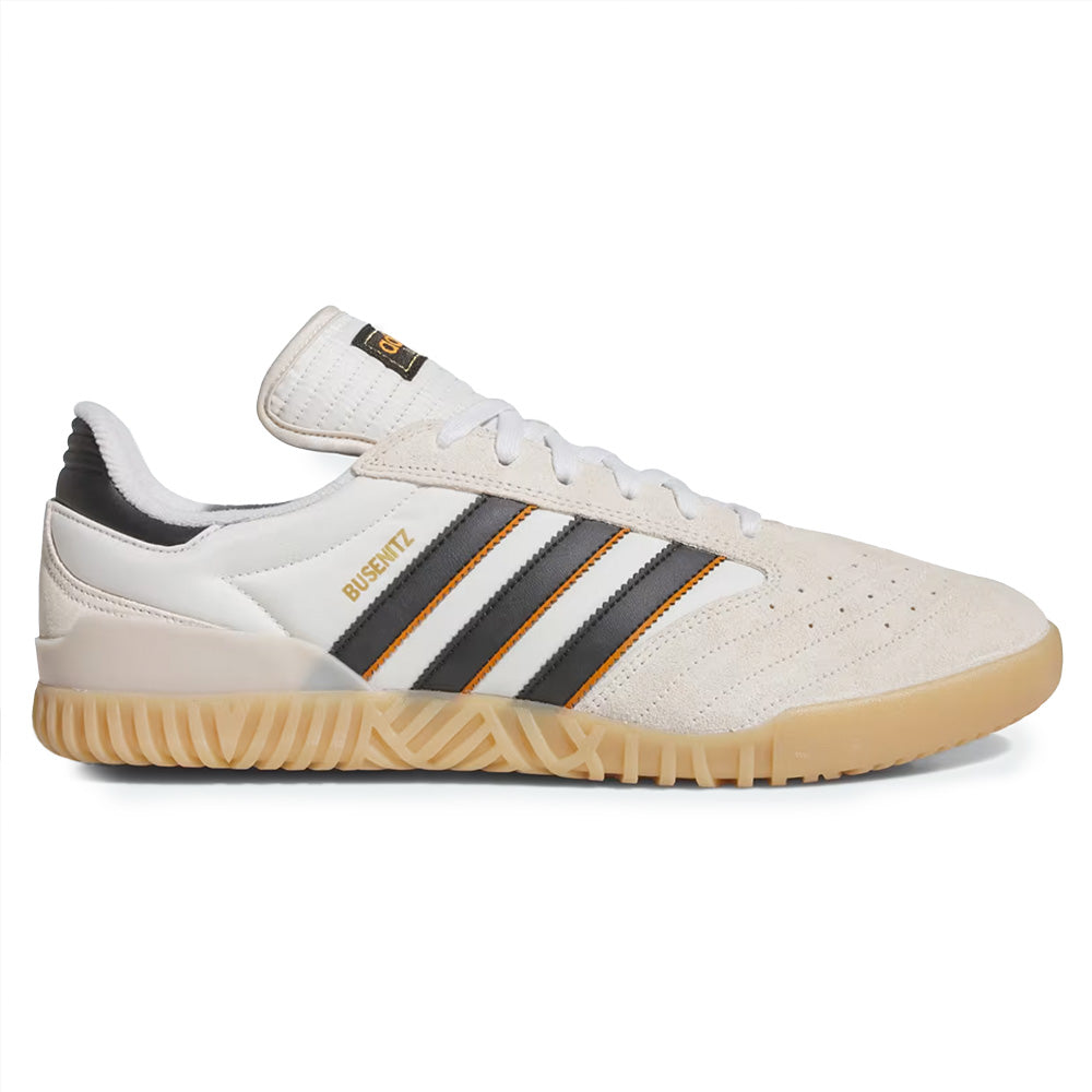 The ADIDAS BUSENITZ INDOOR SUPER features a Bliss, Core Black, and Off White palette with gold accents, gum sole, and suede details, drawing inspiration from modern skateboarding.