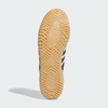 A close-up of the sole of an ADIDAS BUSENITZ INDOOR SUPER in Bliss/Core Black/Off White shows a textured gum rubber outsole with the ADIDAS logo at the center.