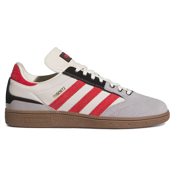 The ADIDAS BUSENITZ BLISS / BETTER SCARLET / GUM is a white skate shoe featuring red stripes, black and grey accents, and a brown gum cupsole, displayed in side profile.