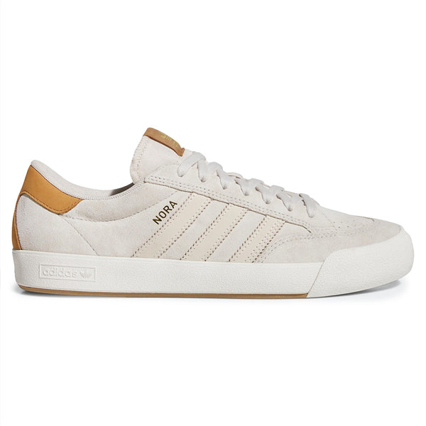 The ADIDAS NORA ALUMINUM / WHITE / GOLD shoe features a modern cupsole design, white sole, tan heel detail, gold "NORA" text on the side, and ADIDAS's signature three stripes.