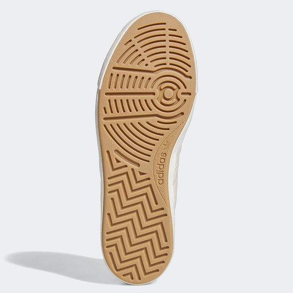 The image shows the bottom view of a beige ADIDAS NORA ALUMINUM / WHITE / GOLD sneaker sole with circular and zigzag tread patterns and the Adidas logo, highlighting its durable skateboarding design.