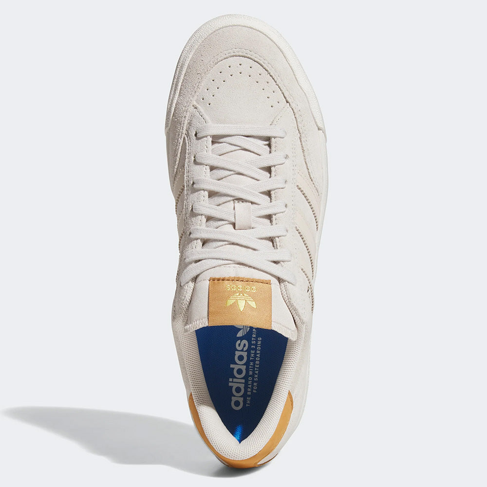 A top view of the ADIDAS NORA ALUMINUM / WHITE / GOLD shoes shows a white sneaker with a tan tongue label, blue insole, and tan heel accent, featuring a modern cupsole design against a plain background.