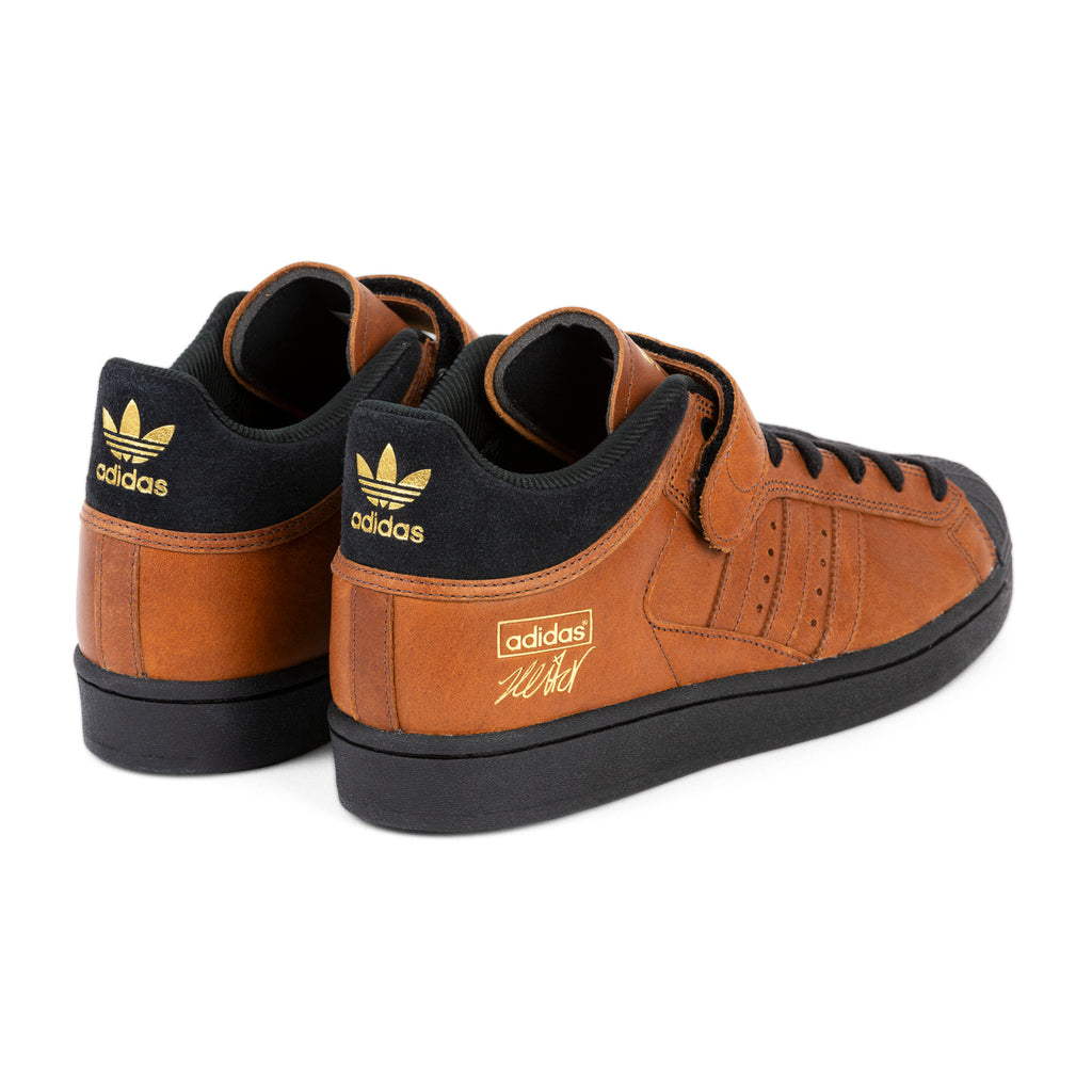 A pair of ADIDAS PRO SHELL ADV X HEITOR dark brown suede sneakers with gold logos on the tongues and heels, displayed against a white background.