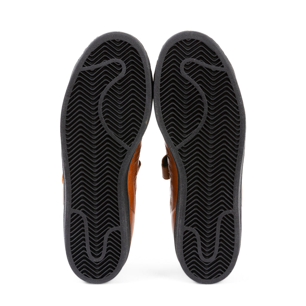 Bottom view of a pair of ADIDAS PRO SHELL ADV X HEITOR dark brown leather flip-flops showing the textured core black soles.