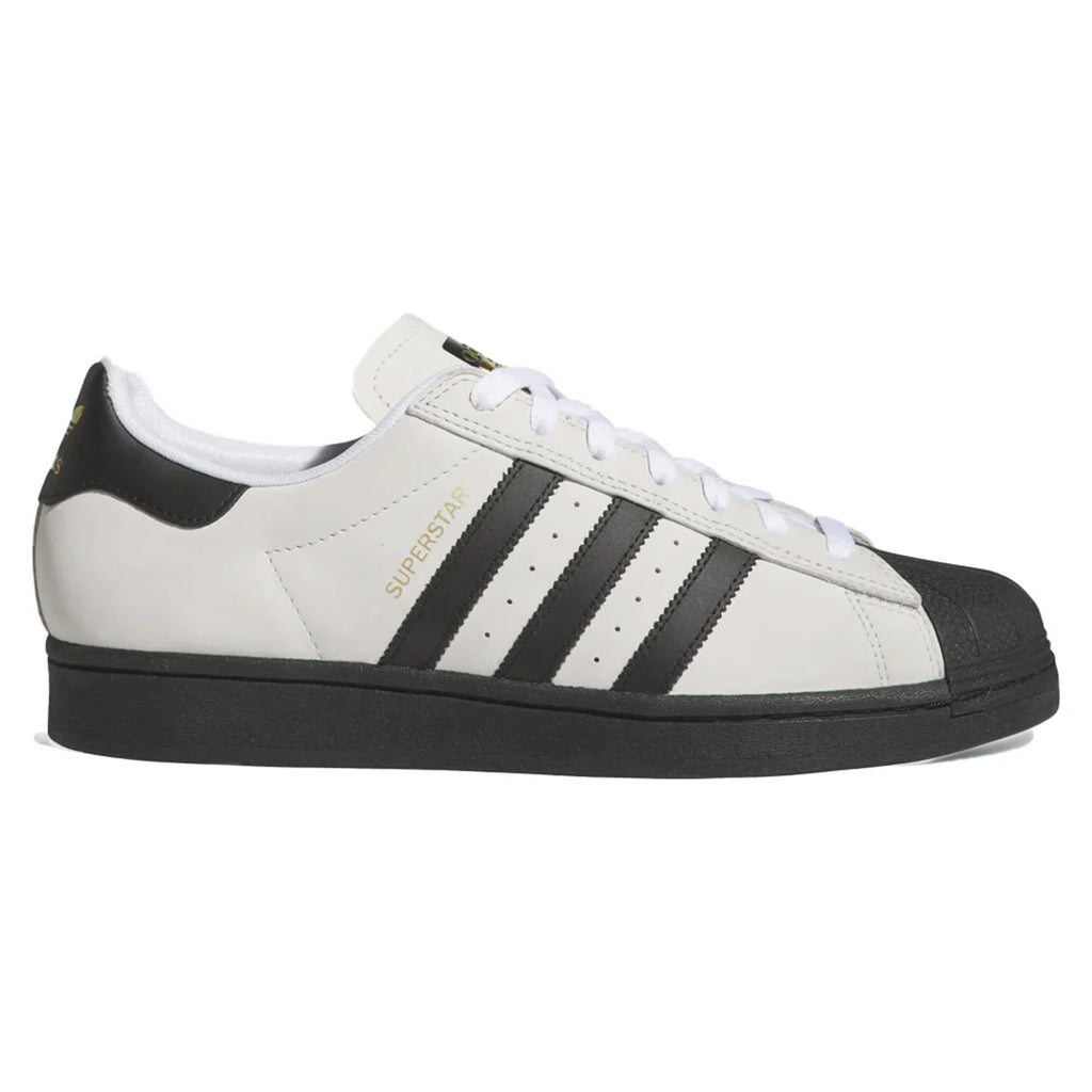 The ADIDAS SUPERSTAR ADV in Crystal White/Core Black features a sleek white design with black stripes and sole. "SUPERSTAR" in gold elegantly adorns its side, while the shoe's suede upper beautifully combines classic style with modern flair.