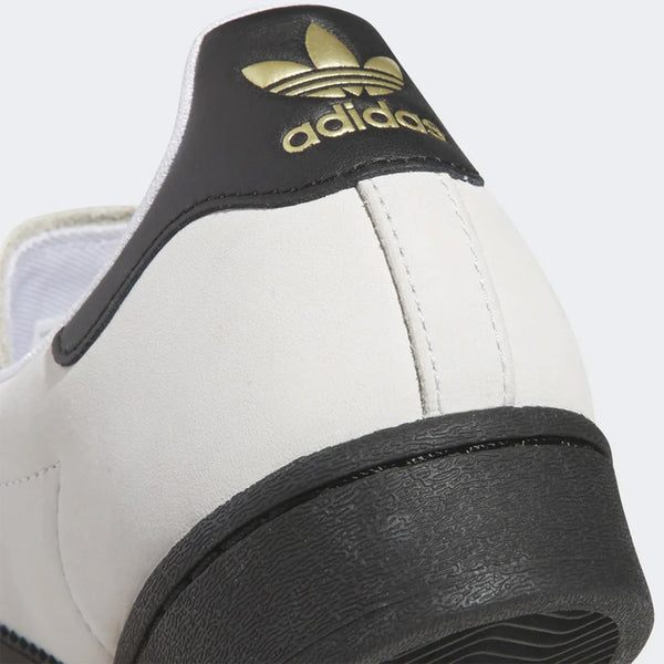 Close-up of the heel of an ADIDAS SUPERSTAR ADV sneaker in Crystal White/Core Black, showcasing the brand name and trefoil logo on the black and gold heel tab. The design includes a flexible cupsole for added comfort and style.