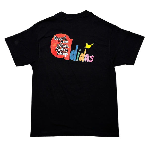 Retro-style black tee, "ADIDAS X BLUETILE X SKATE SHOP DAY GONZ," celebrates Bluetile Skateboards with vibrant text and a yellow skateboard graphic.