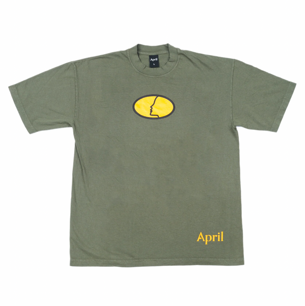 an army green shirt with an orange oval printed on the chest, the april face logo is inside the oval.  the word april is printed in orange puff ink on the bottom left of the shirt