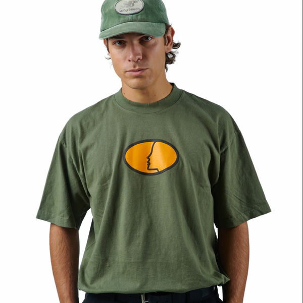 A male model is seen wearing the oversized boxy green shirt tucked into his pants