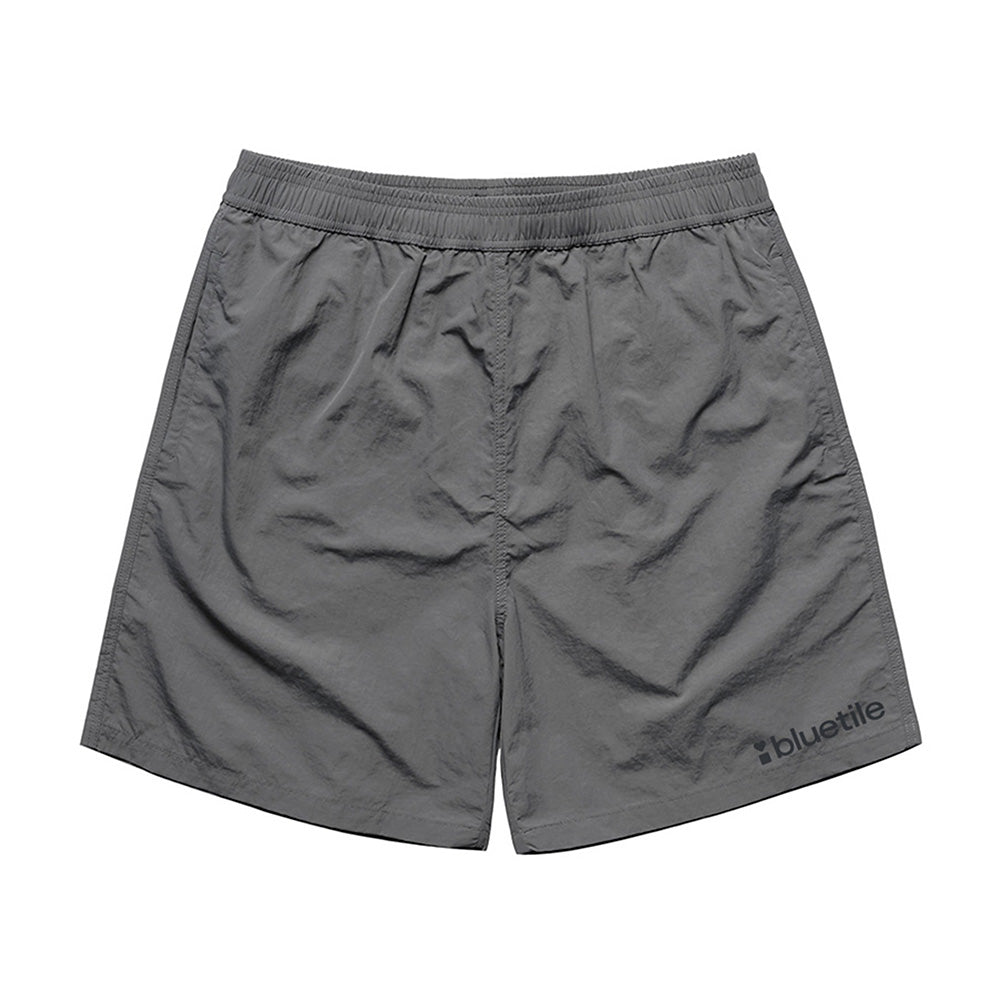 The BLUETILE LOGO SWIM SHORTS SHADOW by Bluetile Skateboards feature quick-dry fabric, an elastic waistband, and a "bluetile" logo printed near the left leg’s bottom hem.