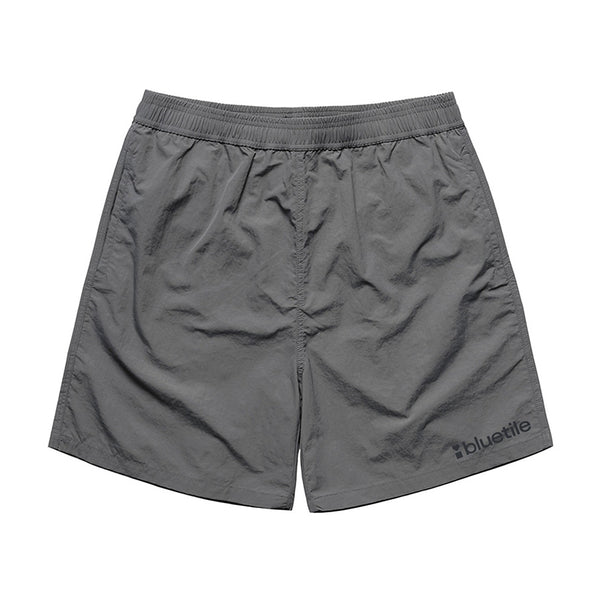 The BLUETILE LOGO SWIM SHORTS SHADOW by Bluetile Skateboards feature quick-dry fabric, an elastic waistband, and a "bluetile" logo printed near the left leg’s bottom hem.