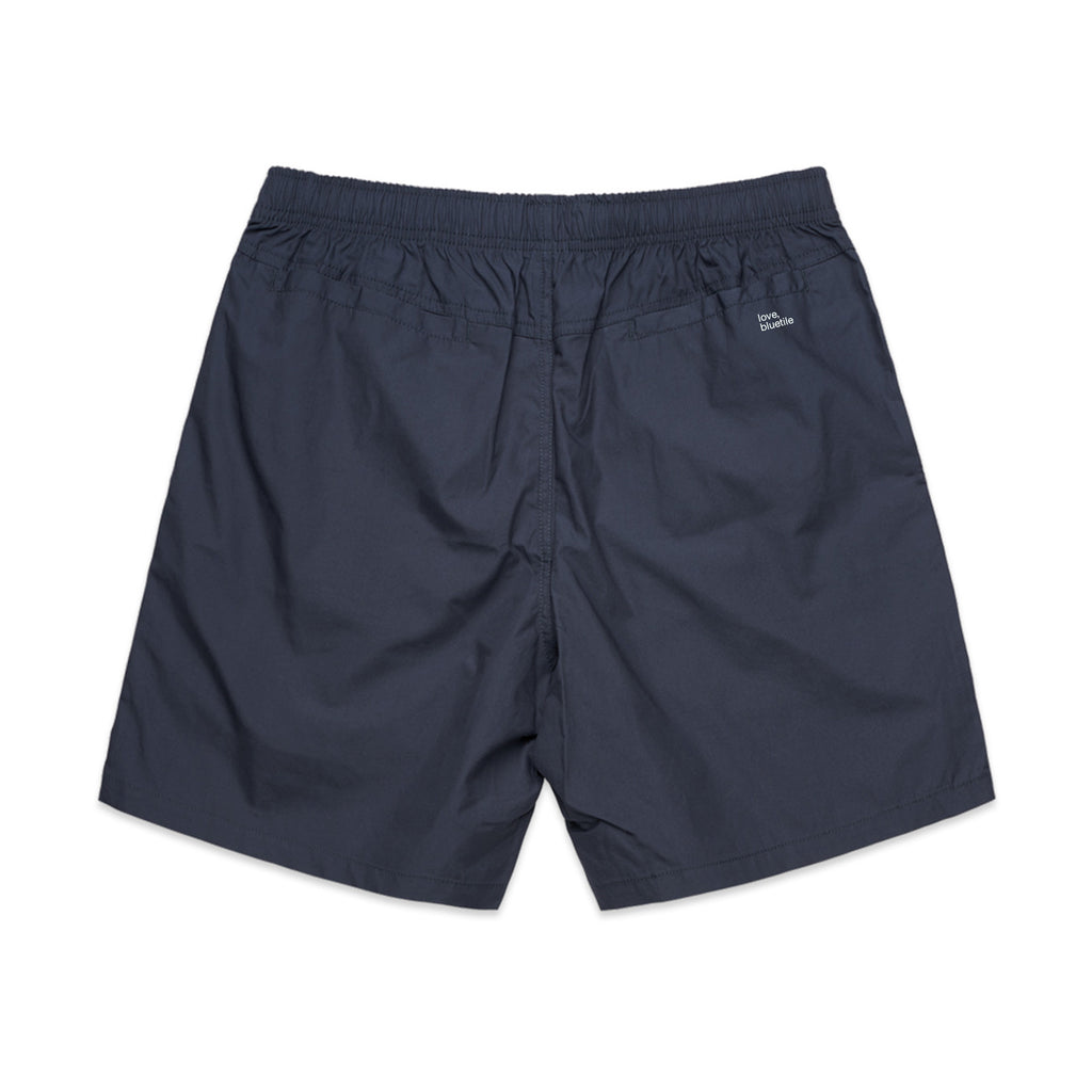 A pair of dark blue, knee-length shorts made from 100% cotton, featuring an elastic waistband and a small BLUETILE SURPLUS V3 BEACH SHORT PETRO BLUE logo on the back from Bluetile Skateboards.