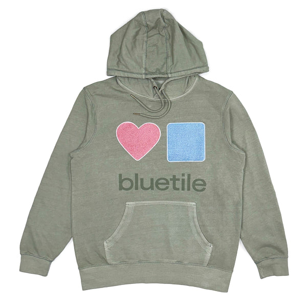 The BLUETILE CHENILLE HEART & SQUARE HOODIE SAGE by Bluetile Skateboards showcases a green design featuring a pink heart and blue square graphic, with the "BLUETILE" text below. It's an ideal choice for those who have a passion for skateboards and style.