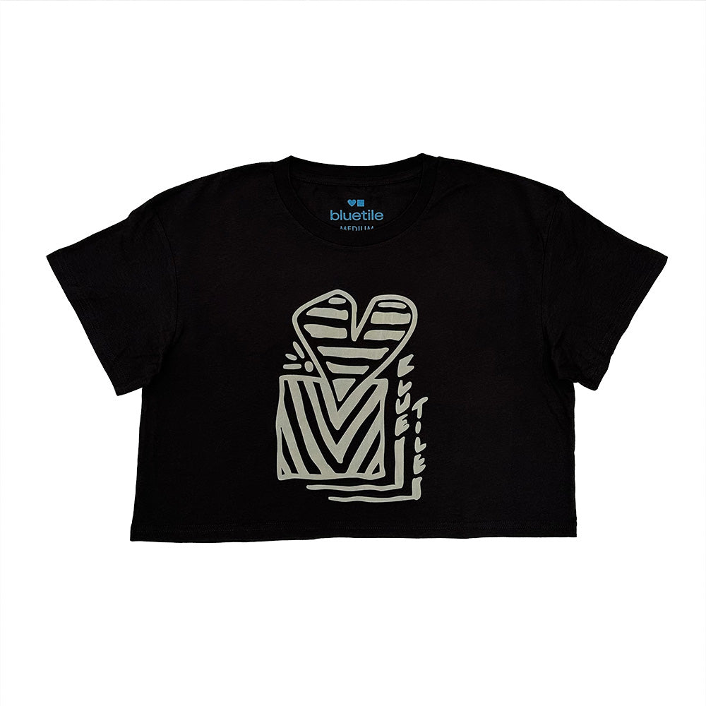 The BLUETILE HEART + SQUARE CROP TEE COAL by Bluetile Skateboards is a relaxed-fit black crop tee with a light abstract heart and geometric print, "bluetile" branding, and crafted from 100% combed cotton for comfort.