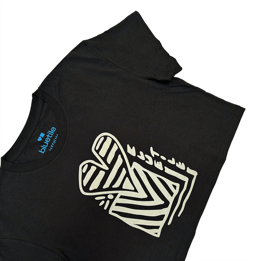 The BLUETILE HEART + SQUARE CROP TEE COAL by Bluetile Skateboards is a black crop tee made from soft combed cotton, featuring a bold white stylized heart and geometric lines graphic on the front and a "bluetile" tag at the collar.