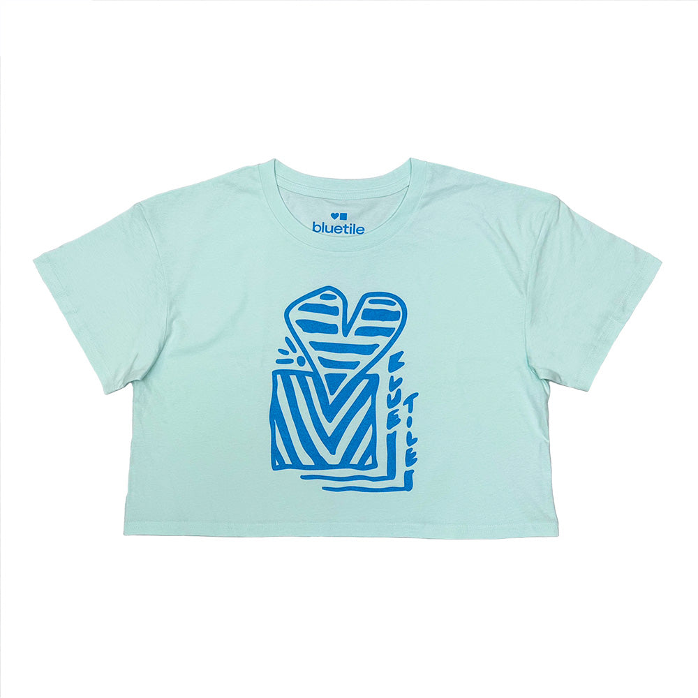 The BLUETILE HEART + SQUARE CROP TEE SEAFOAM by Bluetile Skateboards is a relaxed-fit, light blue 100% combed cotton tee featuring a bold abstract heart and geometric design, with "bluetile" labeled at the neck.
