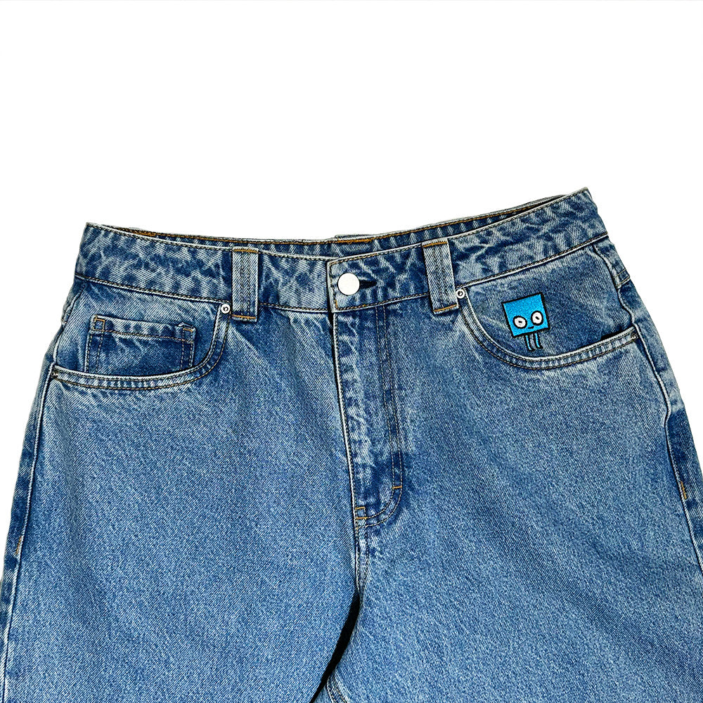 The BLUETILE BRAND DENIM RUTLEDGE PANT BLUE by Bluetile Skateboards features a small blue cartoon face patch above the right pocket, a drawstring adjustable waist, and is shown on a white background.