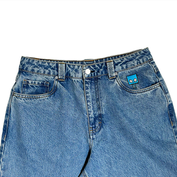 The BLUETILE BRAND DENIM RUTLEDGE PANT BLUE by Bluetile Skateboards features a small blue cartoon face patch above the right pocket, a drawstring adjustable waist, and is shown on a white background.