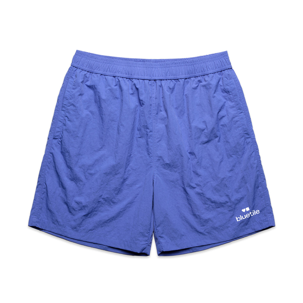 The BLUETILE LOGO SWIM SHORTS LAPIS by Bluetile Skateboards are blue athletic shorts with an elastic waistband and light wrinkling, featuring the BLUETILE LOGO near the bottom hem. Made from recycled nylon, these quick-dry fabric shorts are perfect for active days.