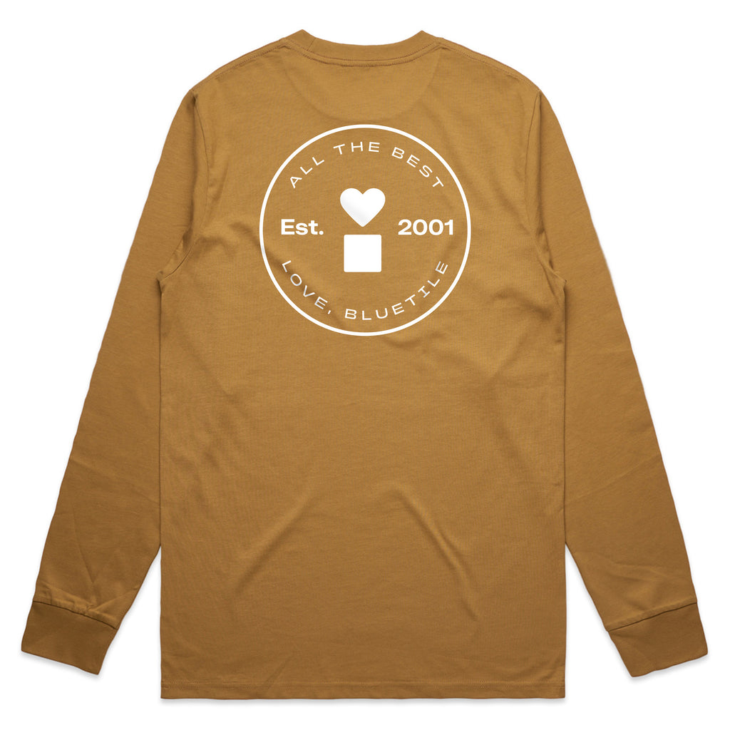 The BLUETILE PRINT STUDIO LONG SLEEVE CAMEL from Bluetile Skateboards is a brown long-sleeve tee made from 100% combed cotton. It features white graphic text that reads: "All the Best, Est. 2001, Love, Bluetile" along with a square and heart design, making it a standout piece from Bluetile Print Studio.