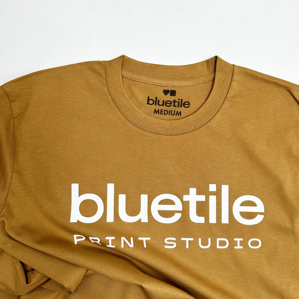 A camel-colored long sleeve tee, crafted from 100% combed cotton, features "Bluetile Print Studio" printed in crisp white on the front.