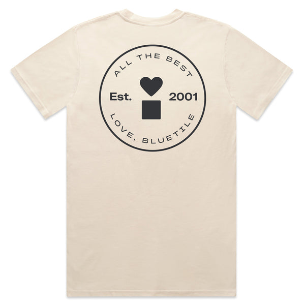 The BLUETILE PRINT STUDIO POCKET TEE ECRU by Bluetile Skateboards is crafted from heavy-weight cotton and available in ecru. It features a circular logo on the back, adorned with a heart and square, alongside hand screen printed text reading "All the Best, Love, Bluetile," and "Est. 2001.