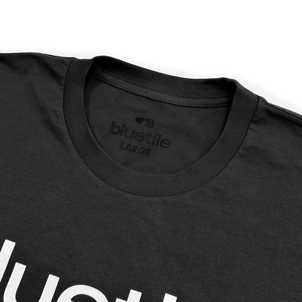 Close-up of a Bluetile Skateboards BLUETILE PRINT STUDIO TEE COAL in "large" size, hand screen printed by Jay Croft. The text in white is partly visible on the front.