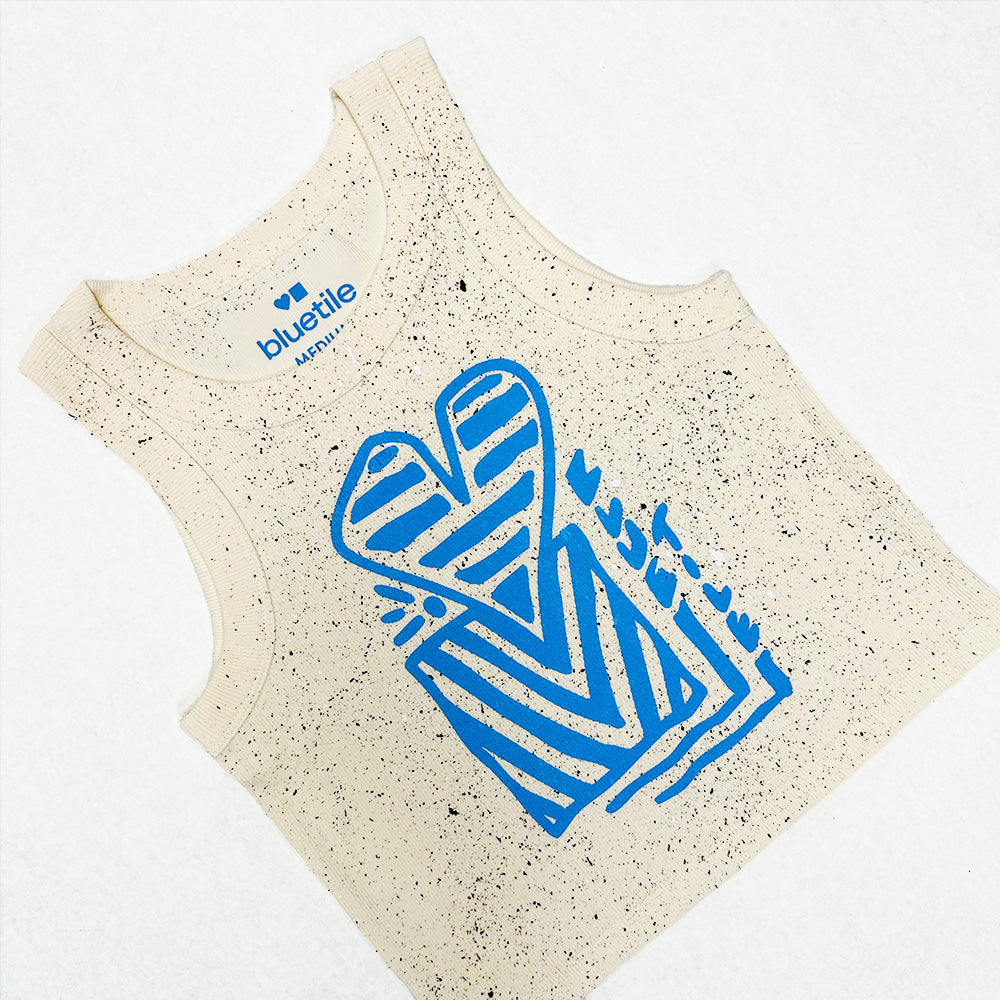 The BLUETILE HEART + SQUARE RIB CROP TANK ECRU by Bluetile Skateboards is a sleeveless beige tank with black speckles, a bold blue abstract front graphic, 100% cotton fabric, and "bluetile ultra soft" label inside the collar.