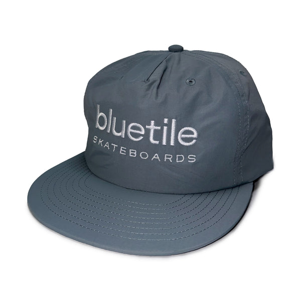 A "BLUE SMOKE" nylon surf hat from Bluetile Skateboards with the "BLUETILE SKATEBOARDS" logo embroidered on the front in white lettering.