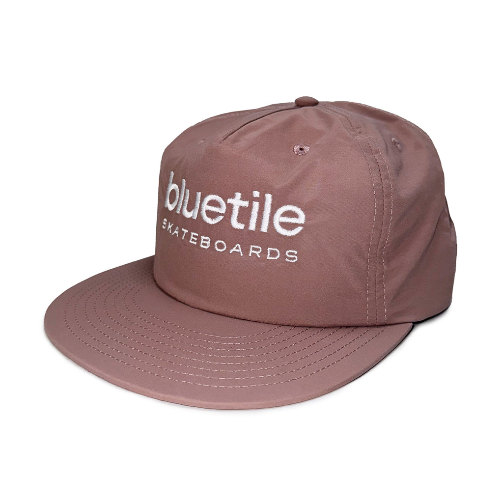 A hazy pink nylon surf hat with "BLUETILE SKATEBOARDS" embroidered in white on the front, photographed against a plain white background.