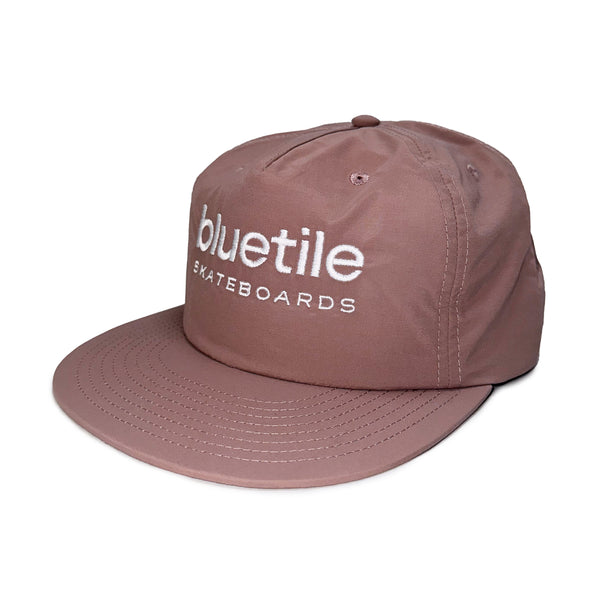 A hazy pink nylon surf hat with "BLUETILE SKATEBOARDS" embroidered in white on the front, photographed against a plain white background.