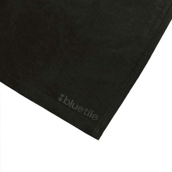 Close-up of the BLUETILE LOGO SWIM SHORTS BLACK by Bluetile Skateboards, showing the lower corner in quick-dry fabric with the subtle dark gray Bluetile logo.