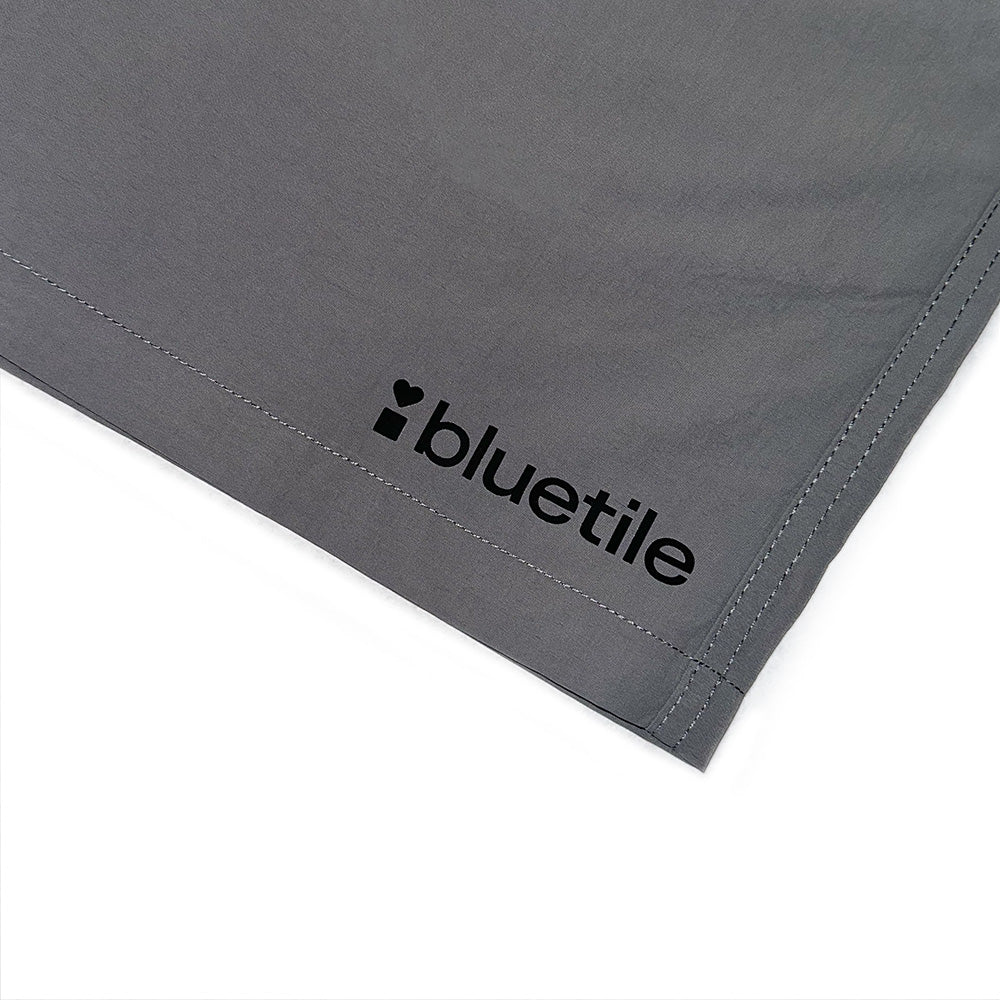 A close-up of the BLUETILE LOGO SWIM SHORTS SHADOW by Bluetile Skateboards shows the gray quick-dry fabric with "bluetile" and a black heart logo printed on the corner.