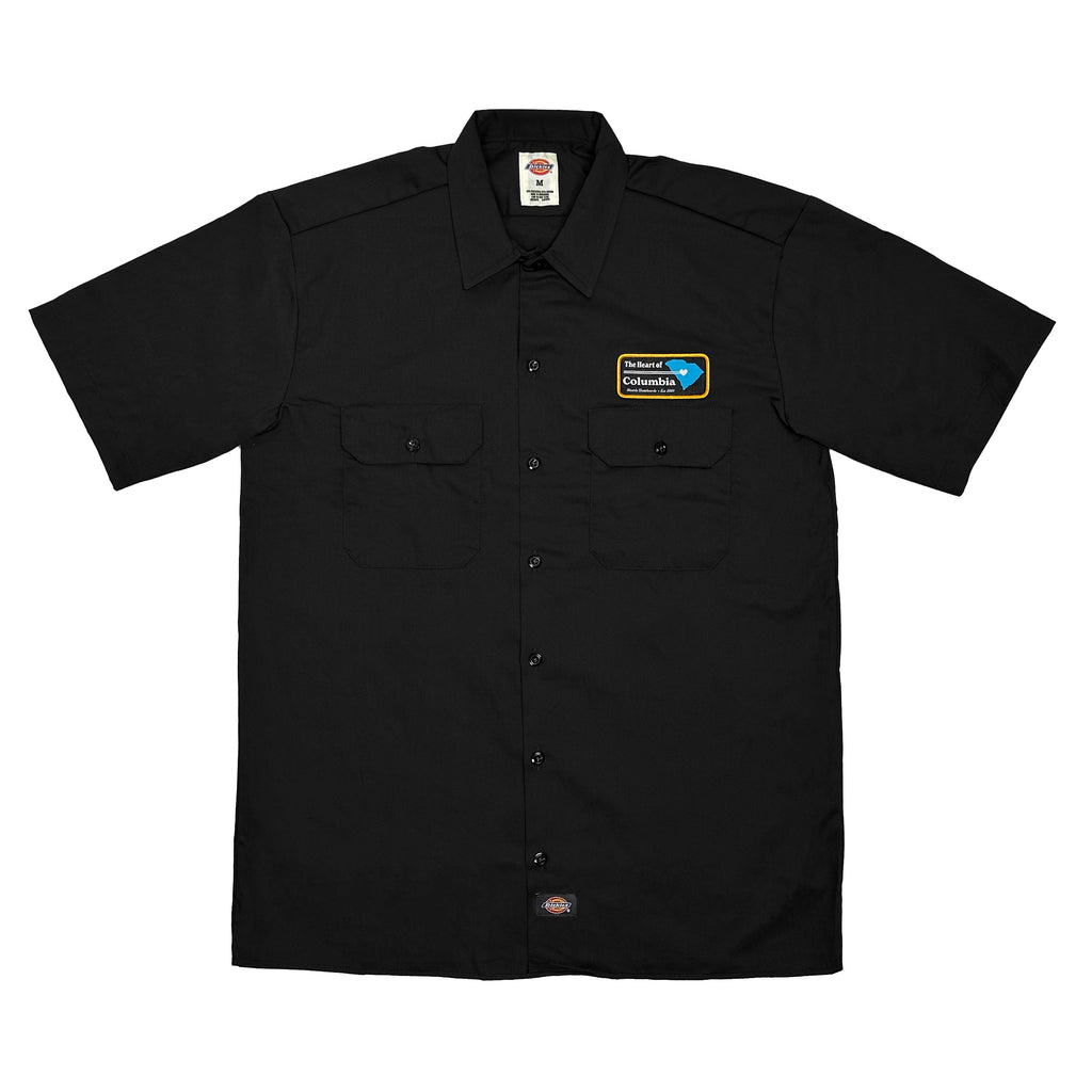 A black Bluetile Skateboards work shirt, named "HEART OF COLUMBIA," featuring short sleeves, two front pockets, and a patch reading “Island Columbia” on the left chest.