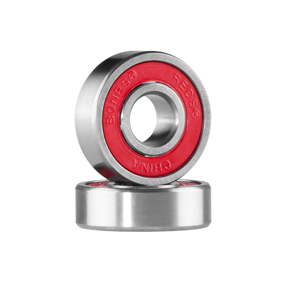 Two metal BONES ball bearings with red seals, from the BONES REDS BEARINGS 8 PACK, stand upright and lie flat. Labeled "Bones Reds China," these are Skate Rated and designed for high speed performance.
