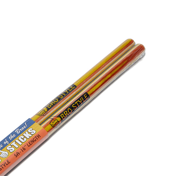Two pairs of BRO STYLE BRO STICKS DRUM STICKS by bro style in colorful yellow and orange packaging, labeled "BBQ Style," are placed diagonally on a white background.