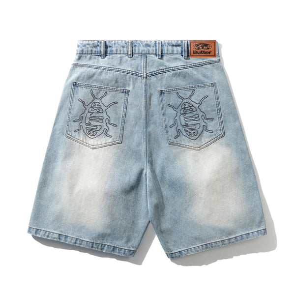 Carpet Co. BUTTER ROACH DENIM SHORTS DISTRESSED INDIGO feature light blue cotton denim, embroidered insect designs on the back pockets, and a brown leather brand patch on the waistband.