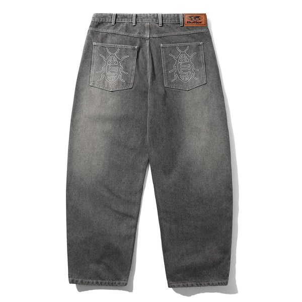 The Butter Goods Roach Denim Jeans Black Wash are shown flat from the back, with embroidered designs on both pockets, a brown leather patch on the waistband, and a signature baggy fit.