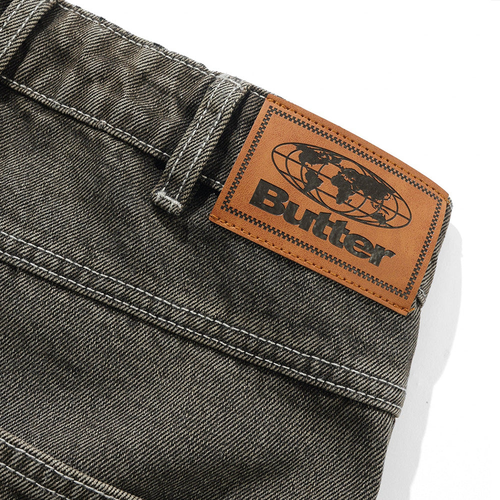 Close-up of BUTTER GOODS ROACH DENIM JEANS BLACK WASH by Butter Goods, featuring a brown leather patch with a world map and "Butter" in bold black lettering, highlighting the brand's signature style.