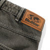 Close-up of BUTTER GOODS ROACH DENIM JEANS BLACK WASH by Butter Goods, featuring a brown leather patch with a world map and "Butter" in bold black lettering, highlighting the brand's signature style.