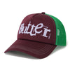 A wine-colored trucker cap with green mesh back panels and the word "Butter" printed in white on the front, from Butter Goods' Breakdown Trucker Cap collection.