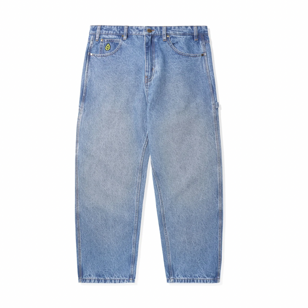 The Butter Goods Weathergear Heavy Weight Denim Jeans in Worn Indigo are high-waisted and light blue, featuring a green patch on the front pocket, and are displayed flat against a white background.